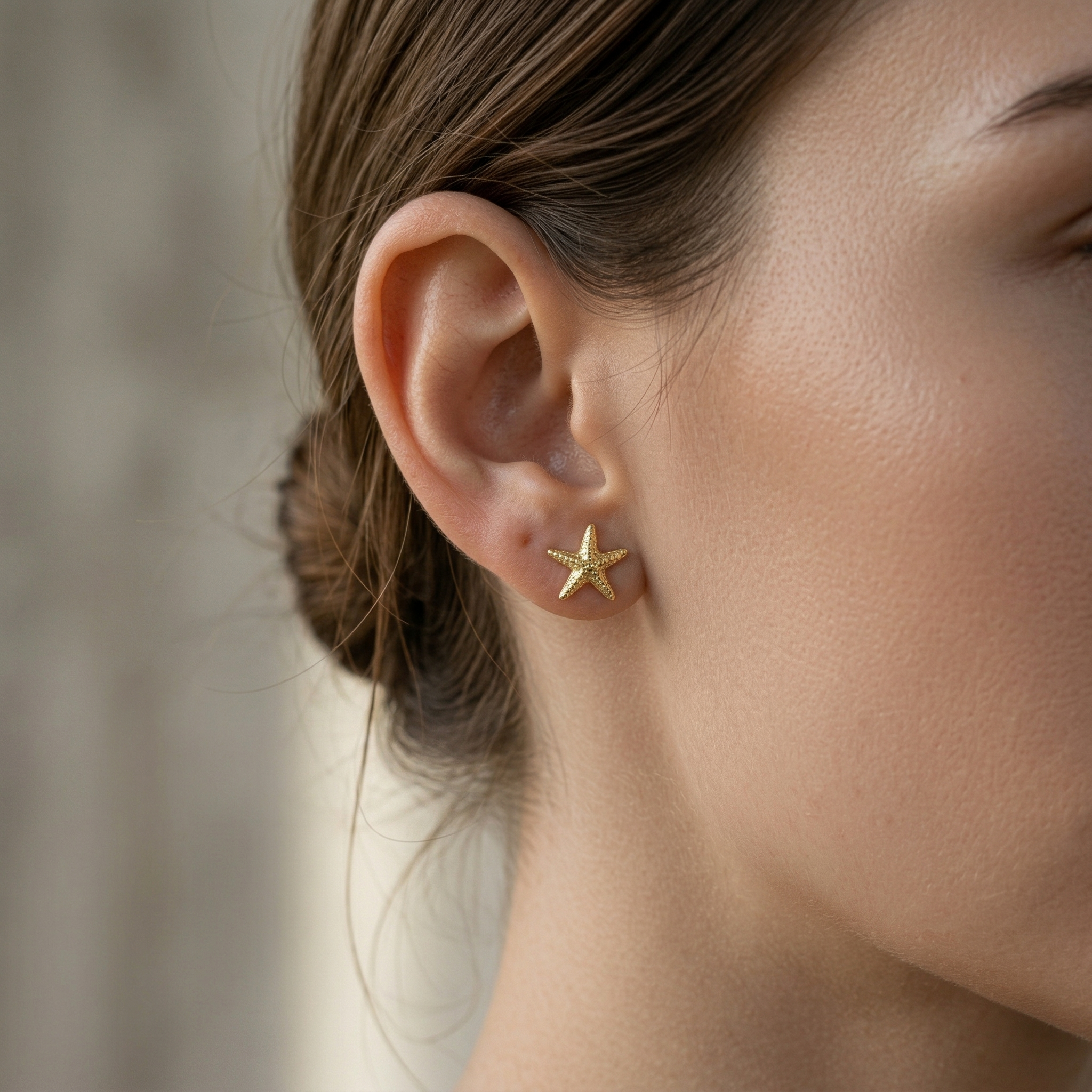 Aretes estrella de mar mini bañados en oro 18K puestos en la oreja