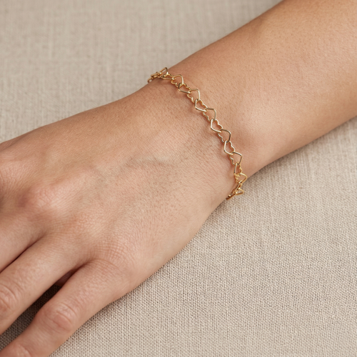 Mujer usando pulsera dorada de corazones de plata 925